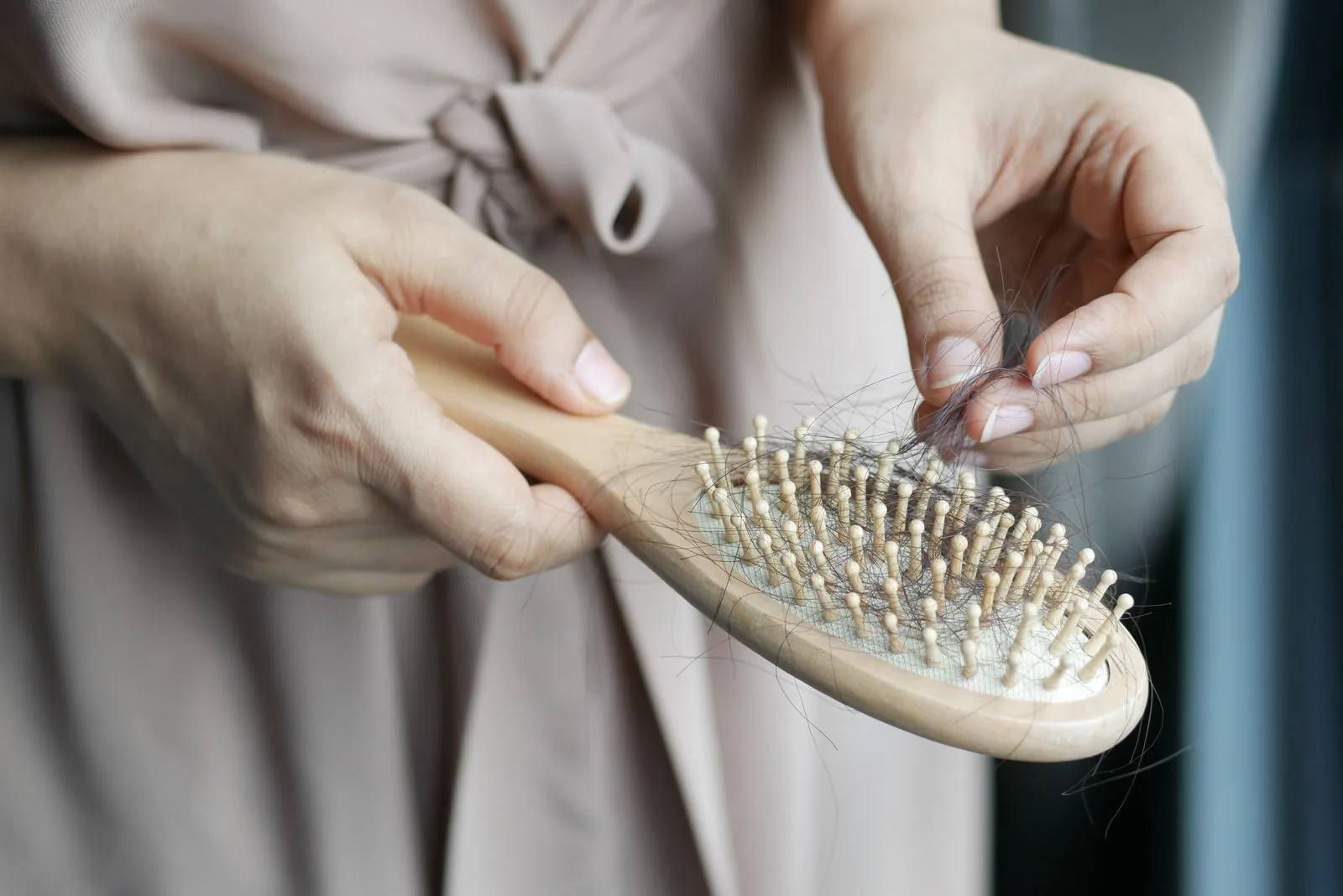 Postpartum hair loss timeline, new mom brushing hair loss into a brush